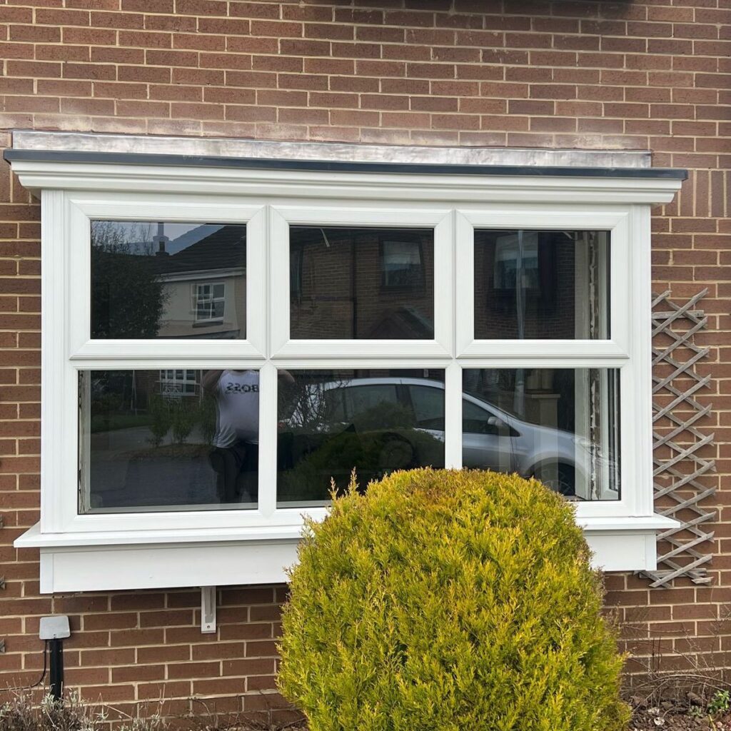 A bow window on the front of a brick house with a bush in front of it.